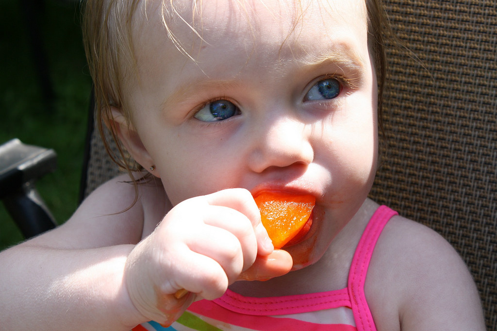 Heat-busting tips for pregnancy through preschool... [Image of a white toddler eating an orange popsicle while sitting in a lawn chair on a hot day.]